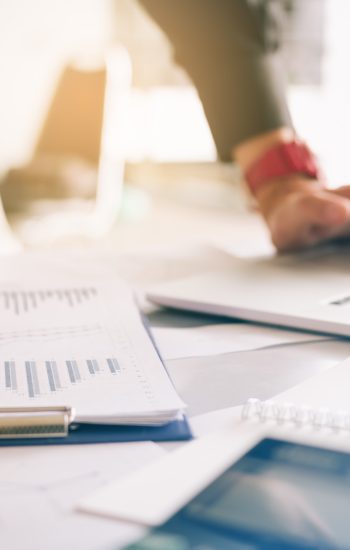 Businessman holding pen and pointing paper chart summary analyzing annual business report with using laptop at room office desk.